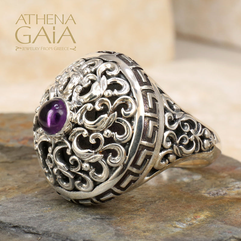 A silver ring featuring a Byzantine-inspired design with a purple amethyst stone, detailed with Greek keys and filigree work.