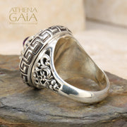 A silver ring featuring a Byzantine-inspired design with a purple amethyst stone, detailed with Greek keys and filigree work.