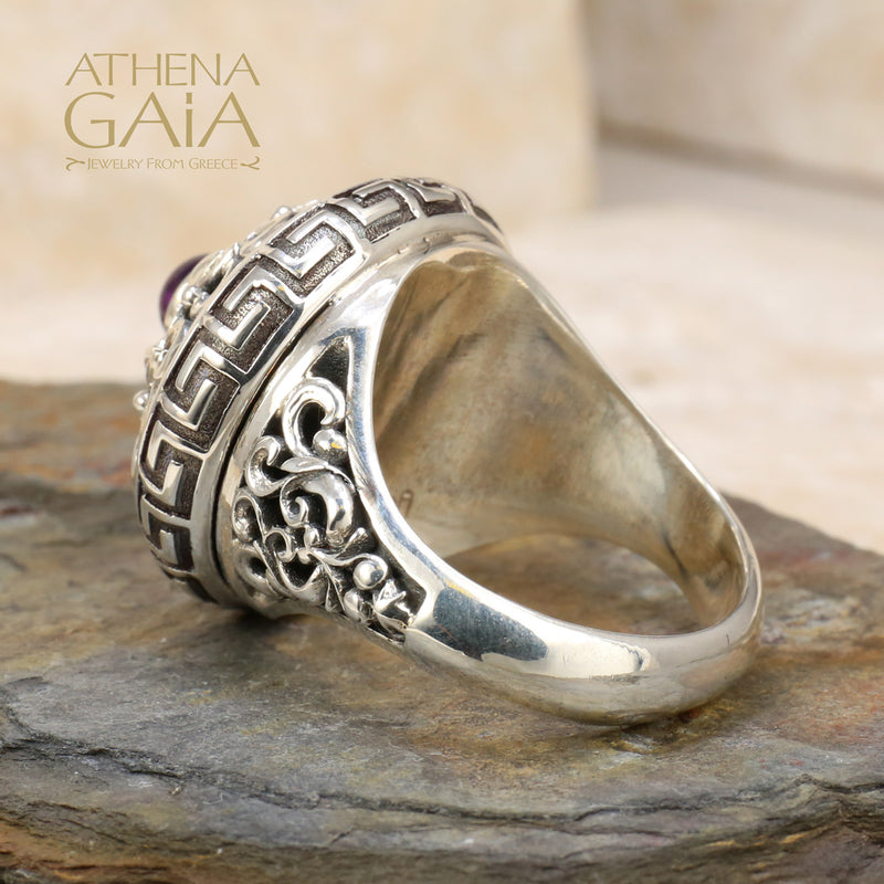 A silver ring featuring a Byzantine-inspired design with a purple amethyst stone, detailed with Greek keys and filigree work.