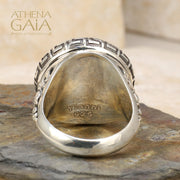 A silver ring featuring a Byzantine-inspired design with a purple amethyst stone, detailed with Greek keys and filigree work.