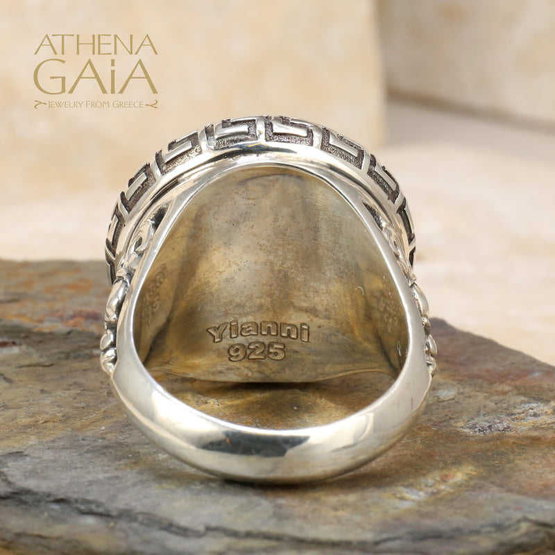 A silver ring featuring a Byzantine-inspired design with a purple amethyst stone, detailed with Greek keys and filigree work.