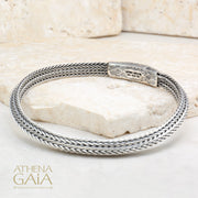 Braided silver bracelet with geometric engraved clasp, handcrafted Greek design on stone surface.