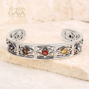 Silver bracelet with colorful stones on a stone surface, branded 'Athena Gaia'.