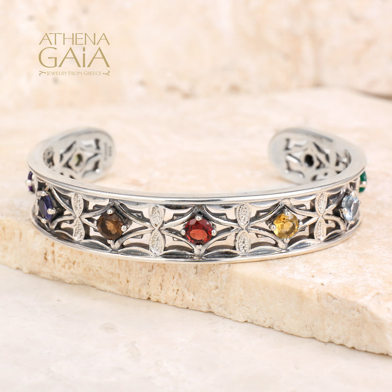 Silver bracelet with colorful stones on a stone surface, branded 'Athena Gaia'.