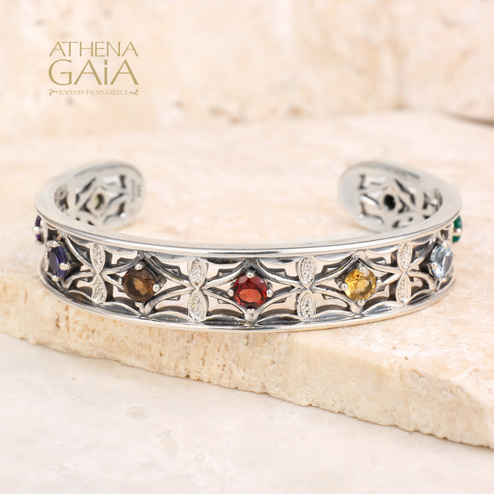 Silver bracelet with colorful stones on a stone surface, branded 'Athena Gaia'.
