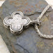 Silver clover shaped pendant featuring a detailed Byzantine style icon on a woven chain necklace.