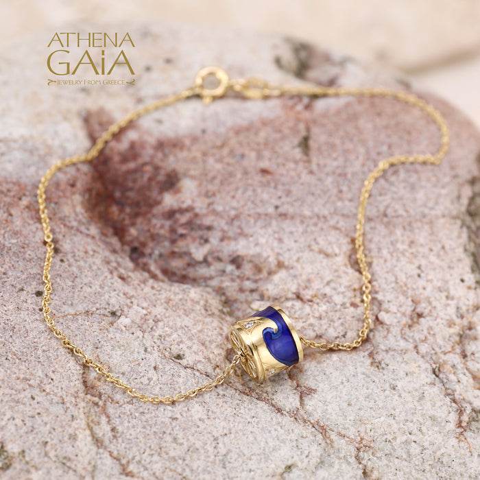 Gold bracelet with blue enamel wave charm centerpiece, displayed on textured stone background.