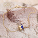 Gold bracelet with blue enamel wave charm centerpiece, displayed on textured stone background.