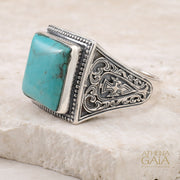 Silver ring with turquoise stone on a beige stone surface, branded 'Athena Gaia'.