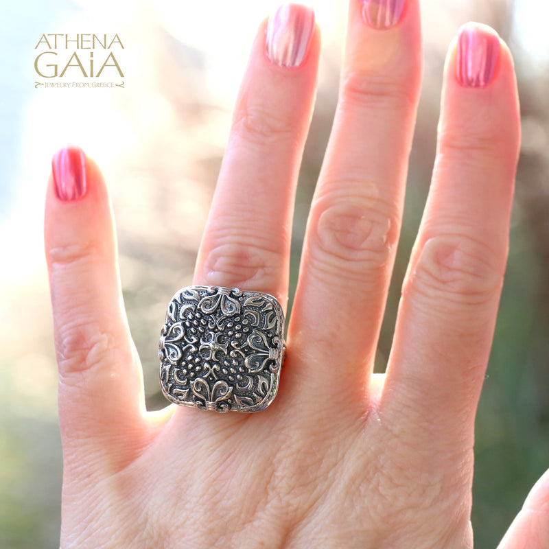 A person wearing a silver unisex ring with a floral pattern on their finger.