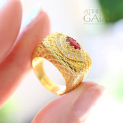 Gold ring with lattice texture and oval ruby centerpiece surrounded by small diamonds, on stone.