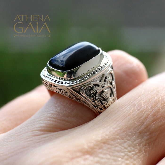 Silver ring with a black stone on a hand, branded 'Athena Gaia'.