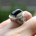 Silver ring with a black stone on a hand, branded 'Athena Gaia'.