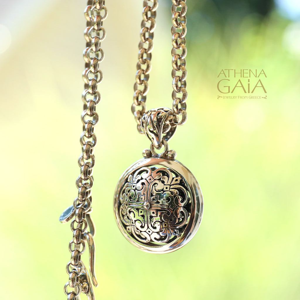 silver rolo chain necklace and pendant with intricate pendant on a blurred green background