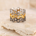 Honeycomb pattern ring in silver and gold tones, displayed on a beige stone with soft lighting.