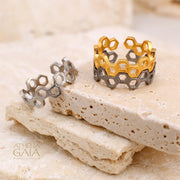 Honeycomb pattern ring in silver and gold tones, displayed on a beige stone with soft lighting.