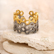 Honeycomb pattern ring in silver and gold tones, displayed on a beige stone with soft lighting.