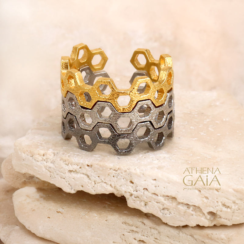 Honeycomb pattern ring in silver and gold tones, displayed on a beige stone with soft lighting.