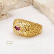 Gold ring with lattice texture and oval ruby centerpiece surrounded by small diamonds, on stone.