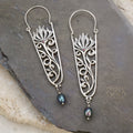 Silver filigree earrings with floral design, red gemstone accents, and blue pearl drops.