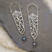 Silver filigree earrings with floral design, red gemstone accents, and blue pearl drops.