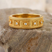 Gold ring with diamond accents on a stone surface, branded 'Athena Gaia'.