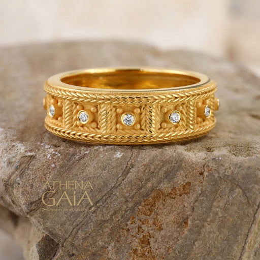 Gold ring with diamond accents on a stone surface, branded 'Athena Gaia'.
