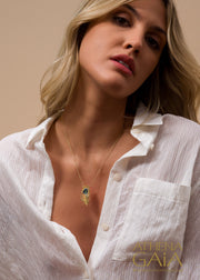 Woman wearing a white shirt with a peacock feather necklace featuring a blue gemstone