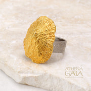 A gold-colored seashell ring displayed on a stone surface with the brand name Athena Gaia visible.