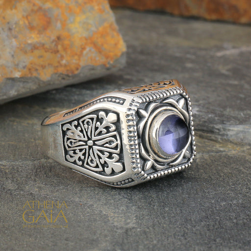 Sterling silver ring with ornate engravings and a faceted purple gemstone set in a detailed square bezel