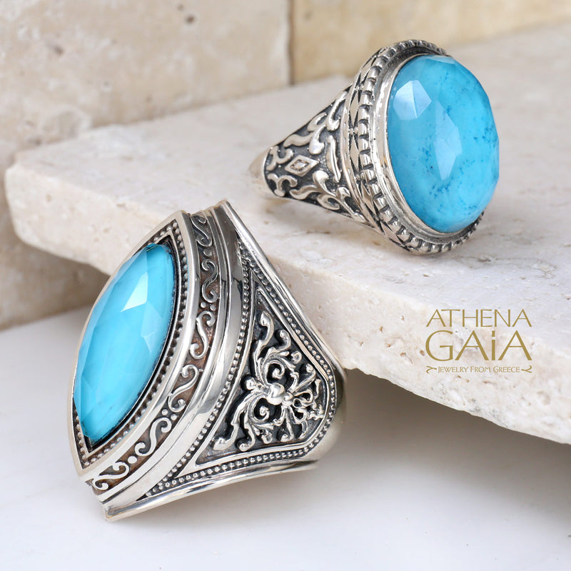 A silver-colored metal ring with a large blue stone set in the center, featuring intricate embossed patterns around the band.