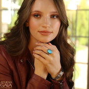 A silver-colored metal ring with a large blue stone set in the center, featuring intricate embossed patterns around the band.