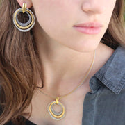A person wearing a silver and gold-colored triple loop earring hoop earrings with a pendant and necklace.