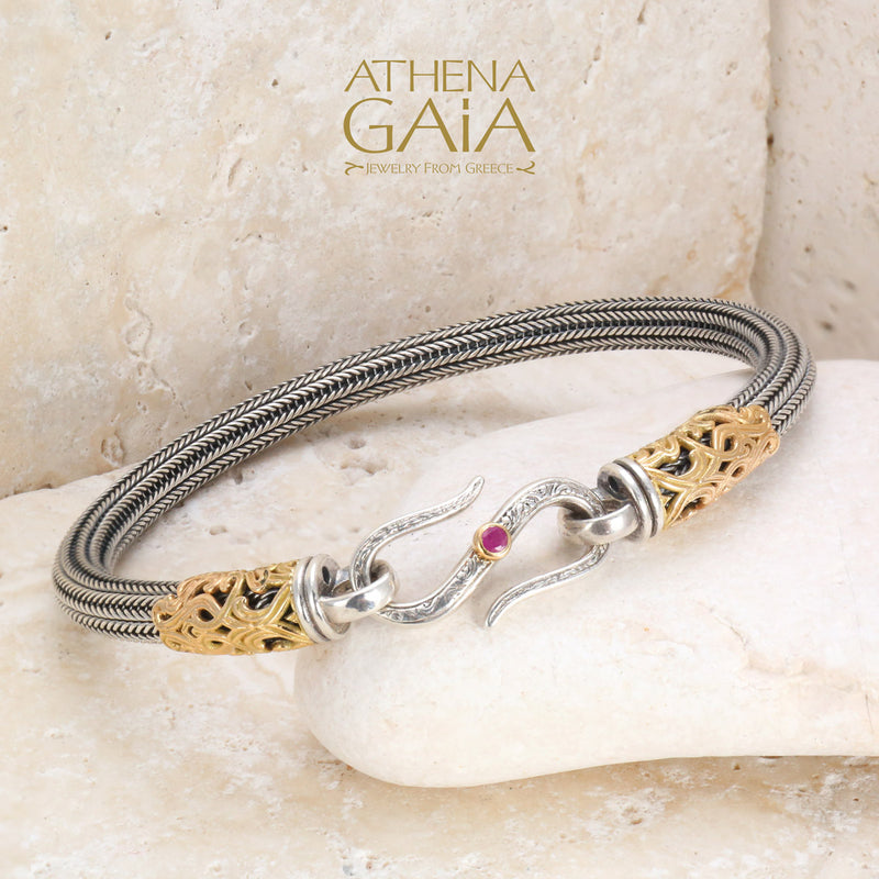 Elegant silver and gold bracelet with ruby-accented hook clasp, handcrafted on cream stone display.