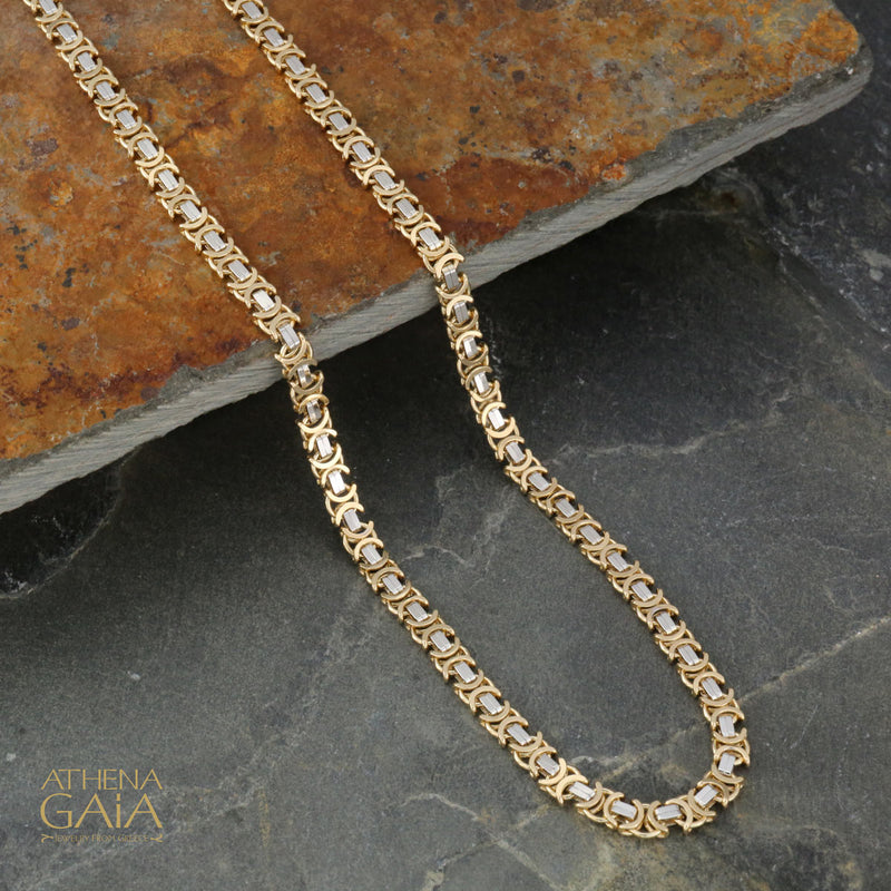 A two-toned yellow and white 14k gold chain laid out on a stone surface.