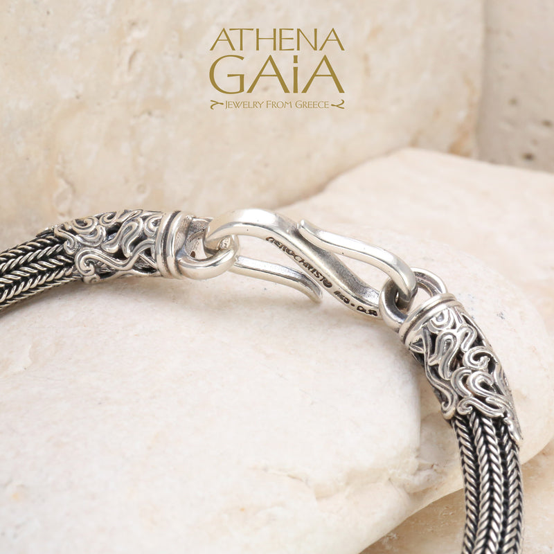 Handcrafted silver bracelet with ornate hook clasp and braided band, resting on beige stone.