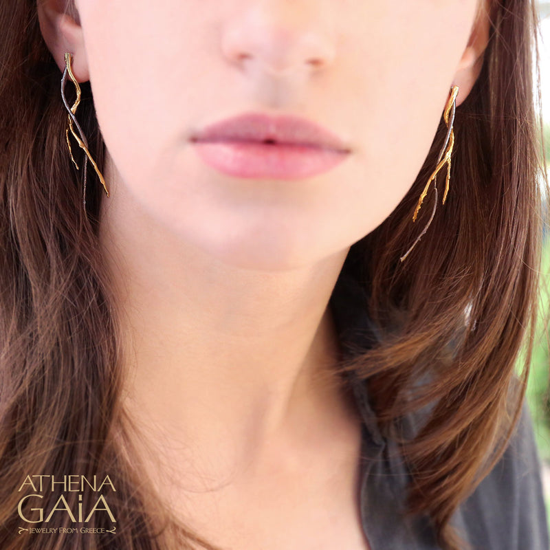A person wearing long branch earrings with a gold plating 